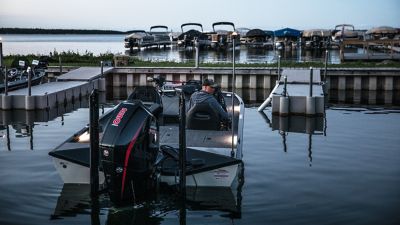 Man backing a Crestliner fishing boat up to a dock, stern view