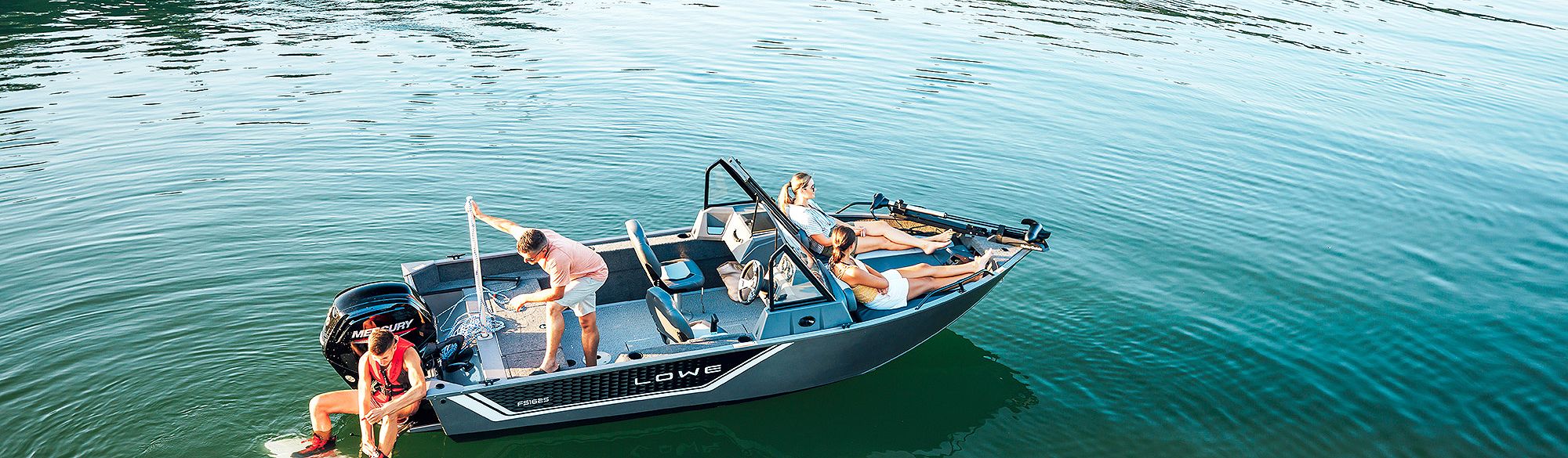 Lowe Fish and Ski Boat, Starboard View, Two Women Sitting in Bow, Man Standing and Wakeboarder Preparing to Ride