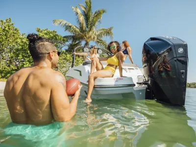 Woman Sitting on Deck of Anchored Bayliner, Two Women in Boat, Man in Water Holding Football