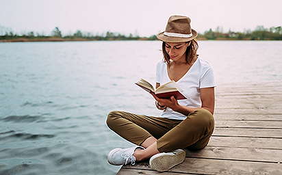 Portrait of a girl reading a book while sitting on a small wooden wharf.