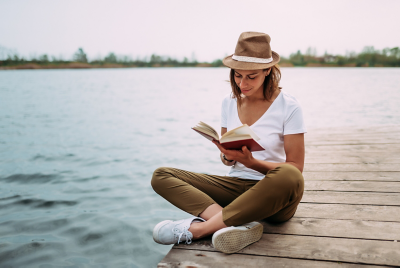 Portrait of a girl reading a book while sitting on a small wooden wharf.