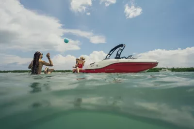 Man Driving Bayliner Deck Boat, Women Riding at Bow and Stern, Starboard View, Boat Underway