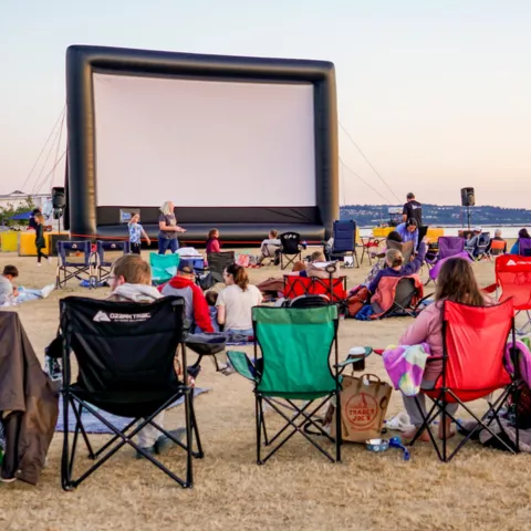 People sitting in chairs on the beach watching a movie