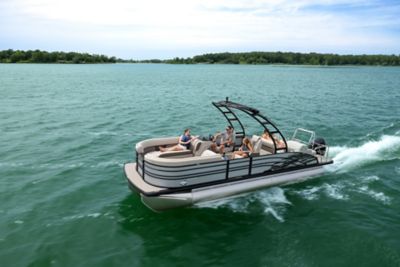 Family lounging on a blue Harris pontoon boat with green trees in the background.