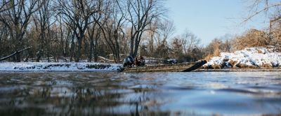 hunter and chocolate labrador retriever on a boat in the water in the winter with snow on the ground