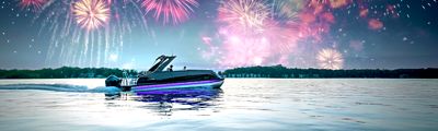 A Harris Pontoon Boat cruising on a calm lake during the evening with fireworks lighting up the sky in various colors. The boat has a sleek design with illuminated blue and purple lights along its side.