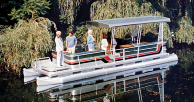 Historic Harris pontoon boat with canopy roof floating on calm water, featuring red, black, and white stripes along the sides. 