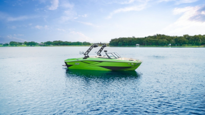 Green H22 wake boat floating in a lake