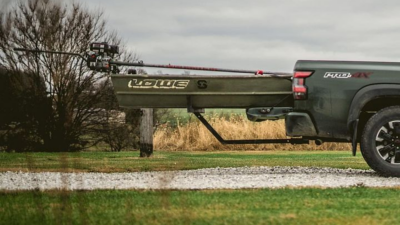 an older green Lowe Jon boat with a motor is loaded onto a dark green truck bed extension on a cloudy day