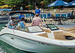 group of people enjoys a conversation on a boat docked at a marina, while a staff member attends to them.