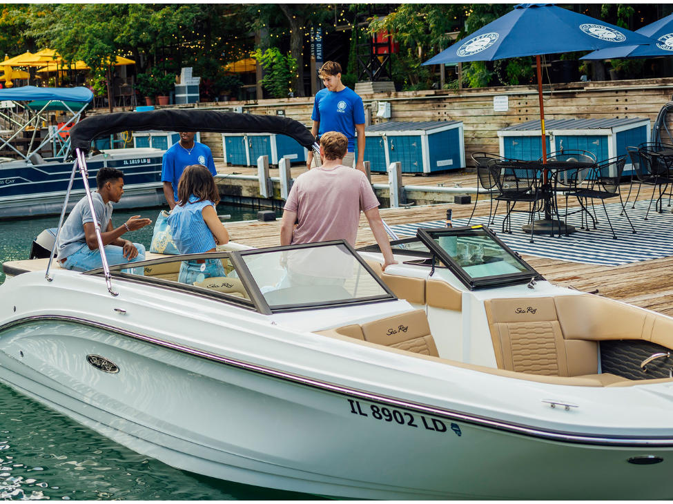 group of people enjoys a conversation on a boat docked at a marina, while a staff member attends to them.